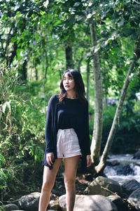 Young woman standing against waterfall in forest