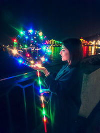 Woman standing by illuminated lights at night