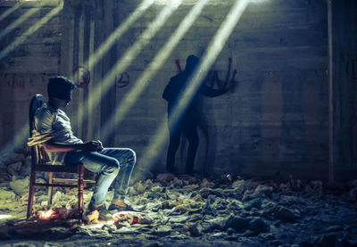 Side view of man sitting on seat against wall