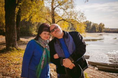 Portrait of mature couple standing in forest by lake during autumn