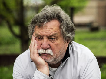 Close-up of sad senior man with hand on chin sitting in park