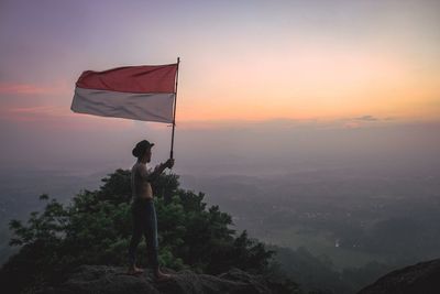 A man with an indonesian flag stands on a mountain enjoying the sunrise