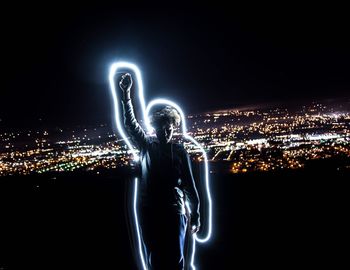 Teenage boy with light painting standing against cityscape at night