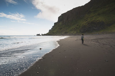 Rear view of woman standing at beach against cliff