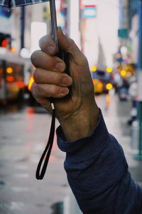 Cropped hand of man holding umbrella in city during rain