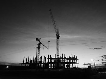 Low angle view of cranes at construction site against sky