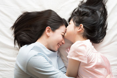 High angle view of daughter kissing happy mother lying on bed