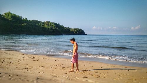 Side view of shirtless man walking on sand at beach