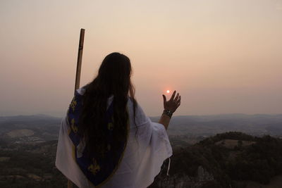 Rear view of woman standing on mountain against sky during sunset