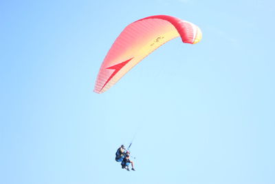 Low angle view of people paragliding against clear sky