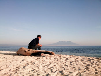 Man sitting at sea shore against sky