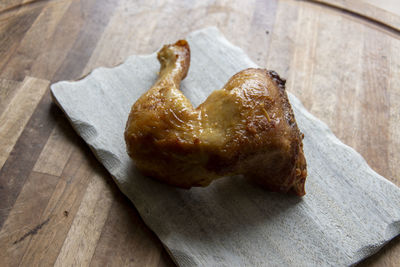 A grilled chicken leg with beautiful crispy skin lies on a wooden board.