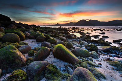 Rocks on beach against sky during sunset