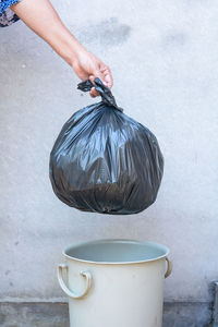 Cropped hand of person holding garbage bag over bin