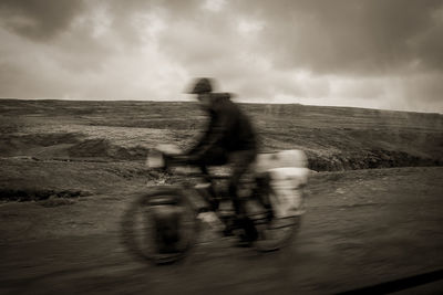 Blurred motion of man riding motorcycle on sea shore against sky