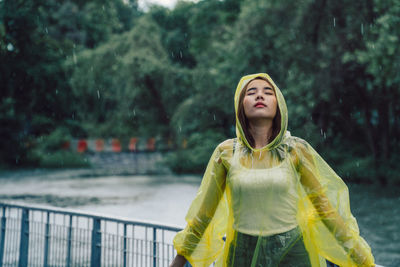 Young woman with eyes closed standing by lake during rainfall