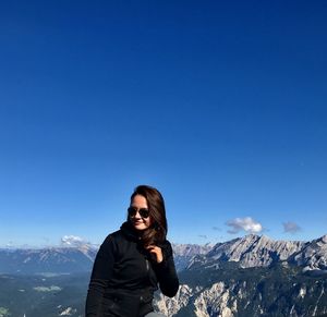 Portrait of man standing on snowcapped mountain against blue sky