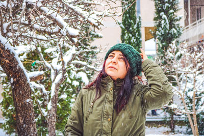 Woman looking away while standing against tree outdoors