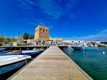 Sailboats moored at harbor against blue sky