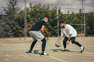 Male friends playing basketball at sports court