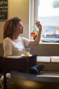 Woman spraying on her face while sitting at restaurant