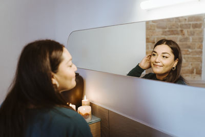 Smiling woman looking at refection in mirror at home