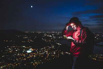 Woman standing by illuminated cityscape against sky at night