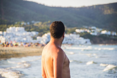 Side view of shirtless man standing at beach during sunset