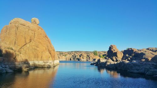 Rock formations by sea against clear blue sky