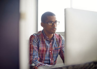 Portrait of young man using mobile phone while standing in office