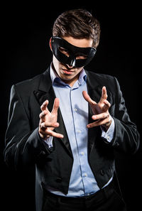 Portrait of man in mask gesturing while standing against black background