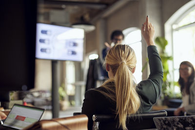 Rear view of blond businesswoman raising hand during meeting