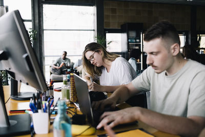 Young businessman working on laptop by female colleague in office
