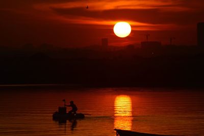 Silhouette people on shore against orange sky during sunset