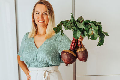 Young woman holding beetroots with green leaves and smiling at camera