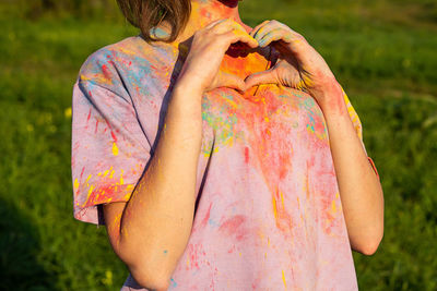 Woman making a heart gesture with her fingers, in t-shirt covered colourful holi powder paint.