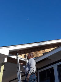 Low angle view of man standing against building against clear blue sky