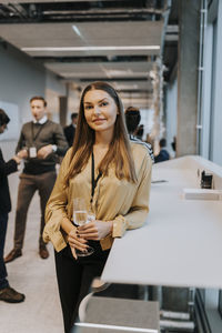 Portrait of smiling businesswoman with champagne flute standing by table during conference