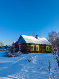 House on snow covered landscape against clear blue sky