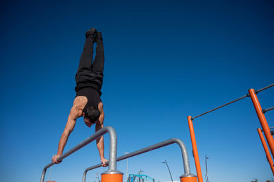 Low angle view of man climbing on field against clear blue sky