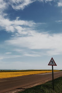 Road sign on field against sky