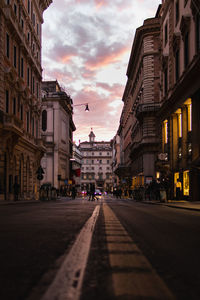 Street amidst buildings against sky at sunset