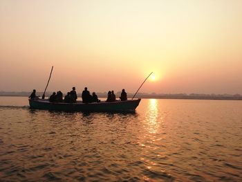 Silhouette people on boat sailing in river against sky during sunset