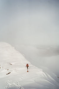 Man skiing on snow covered landscape against sky