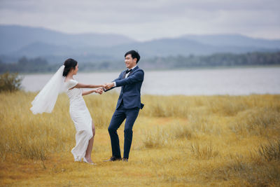 Full length of newlywed couple holding hands outdoors