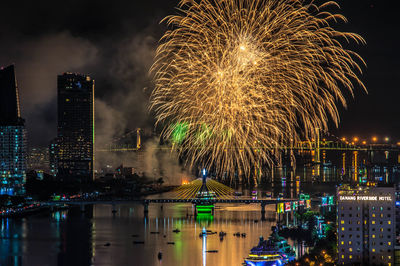 Firework display over illuminated buildings and river in city at night