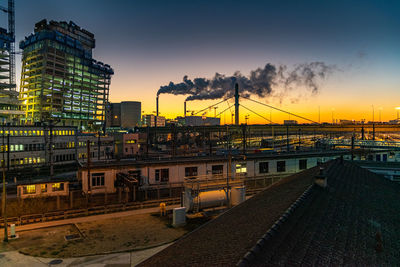 Railroad tracks by buildings against sky during sunset