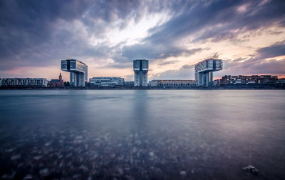 Sea by buildings against sky during sunset in city