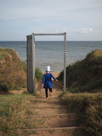 Rear view of man standing on beach against sky