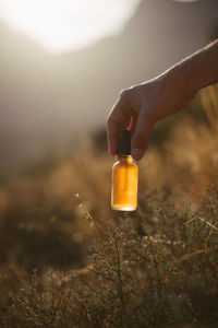 Close-up of woman holding glass bottle on field